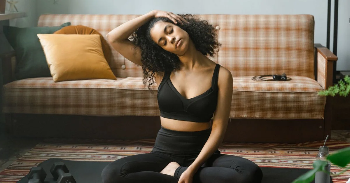Femme en vêtements de sport effectuant un étirement du cou sur un tapis de yoga à l'intérieur, promouvant un mode de vie sain.