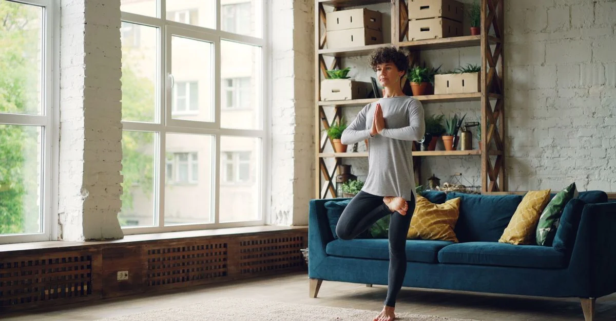 Une femme fait du yoga dans un salon lumineux et chaleureux avec des plantes et de la lumière naturelle.